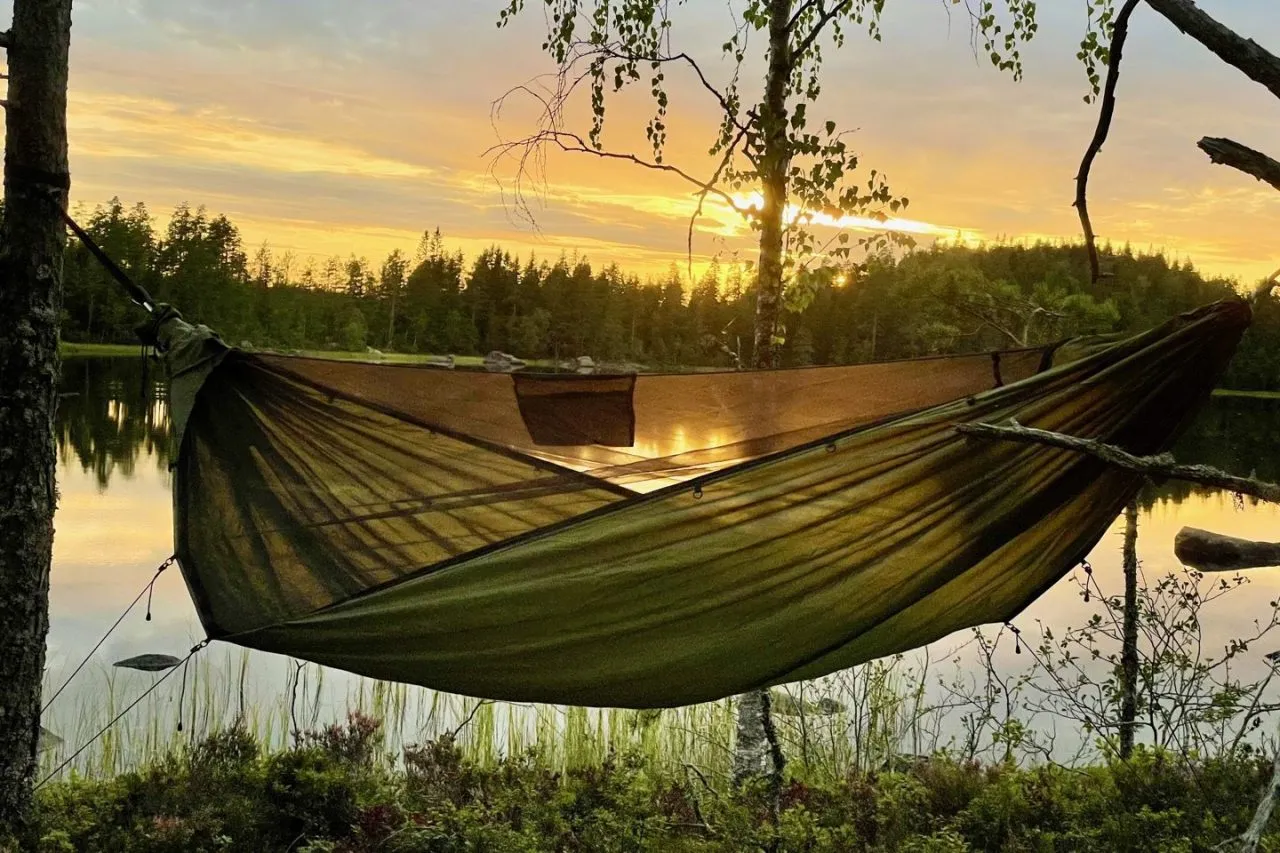 A Momo Jord hammock hung between two trees by a Nordic lake